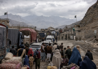 Crowded mountain border crossing with trucks, civilians, security guards, and Pakistani flags