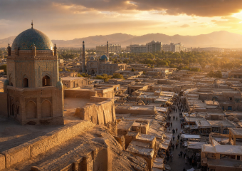 Sunset view over an ancient city with turquoise-domed Islamic architecture, a bustling market, and mountains in the distance