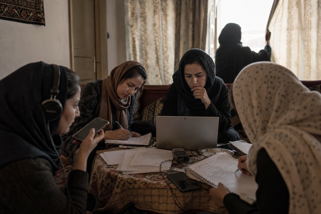 Women collaborate around a laptop, handwritten notes, and recording equipment at a table