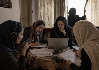 Women collaborate around a laptop, handwritten notes, and recording equipment at a table