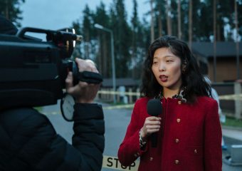 Asian female journalist reporting live from a suburban crime scene with camera and microphone.